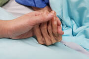 A picture of a person holding an older person's hand who is in the hospital