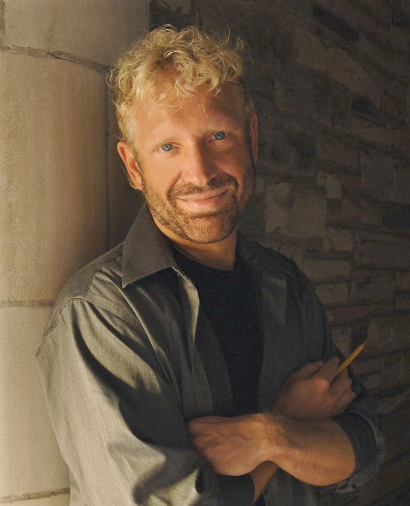the composer Michael Kurek stands with a pencil in his hand; he is strawberry blonde with bright blue eyes and a darker blonde beard