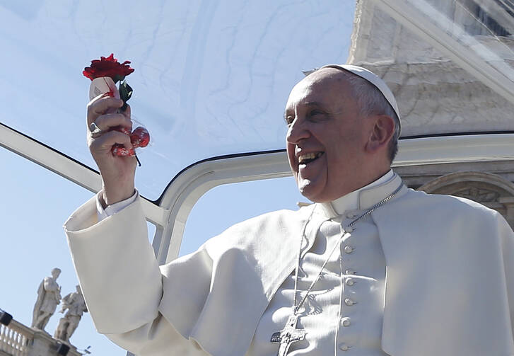 Pope Francis holds a rose and chocolates thrown by a person in the crowd as he arrives for an audience for engaged couples in St. Peter's Square at the Vatican Feb. 14, Valentine's Day. (CNS photo/Paul Haring) 