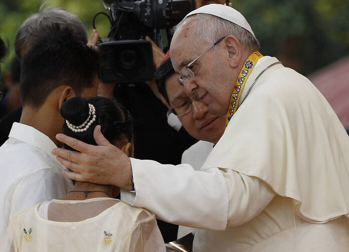 Pope Francis comforts former street child who spoke during meeting with young people at university in Manila.
