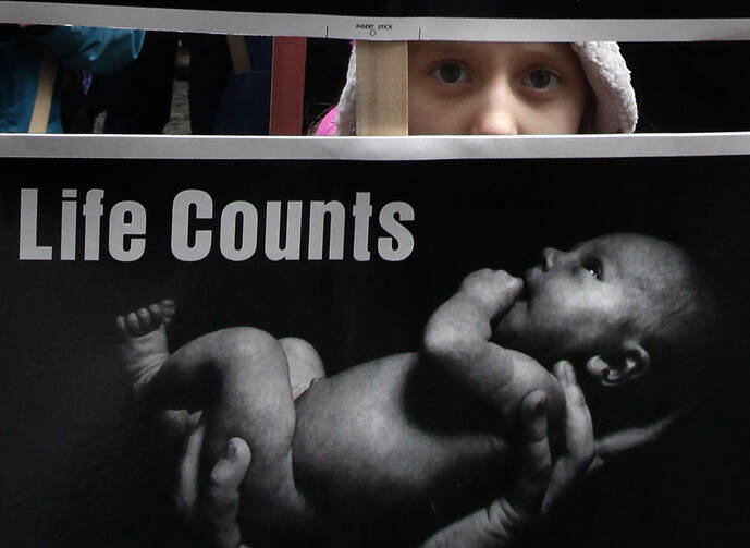 A young girl peeks through signs she is holding as she walks through downtown Chicago during the city's Jan. 18 March for Life. The marchers were calling for an end to abortion. (CNS photo/Karen Callaway, Catholic New World) 
