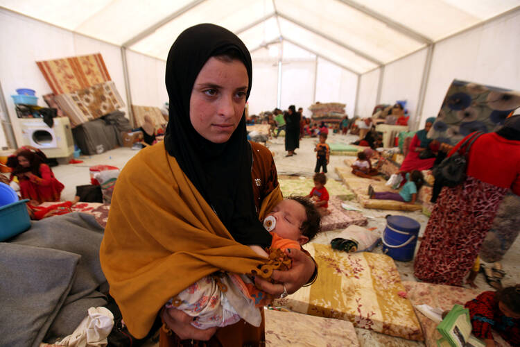 A displaced woman carries her sleeping child June 15 at a refugee camp near Mosul, Iraq. (CNS photo/Azad Lashkari, Reuters)