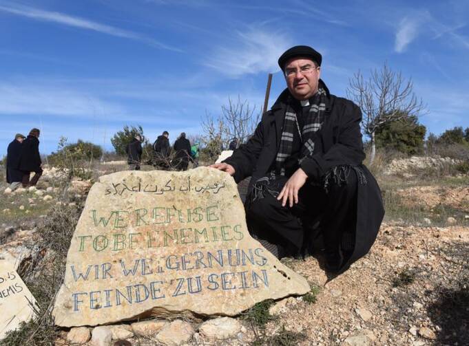 Bishop Oscar Cantu of Las Cruces, N.M., kneels by a stone that reads "We Refuse To Be Enemies" Jan. 16 at the entrance to the Tent of Nations in the West Bank, near Bethlehem. (CNS photo/Debbie Hill)
