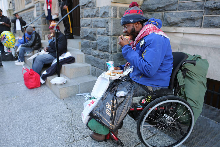 Able Putu, a homeless man in a wheelchair, eats a meal on a Washington street March 8 prepared by volunteers of the St. Maria's meals program run by Catholic Charities. Catholic Charities agencies across the United States could face huge budget holes in other areas should Congress approve the president’s proposed budget. (CNS photo/Chaz Muth)