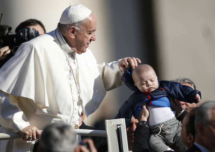 Pope Francis adjusts the hoodie of a baby during his general audience in St. Peter's Square at the Vatican on March 29. (CNS photo/Paul Haring)