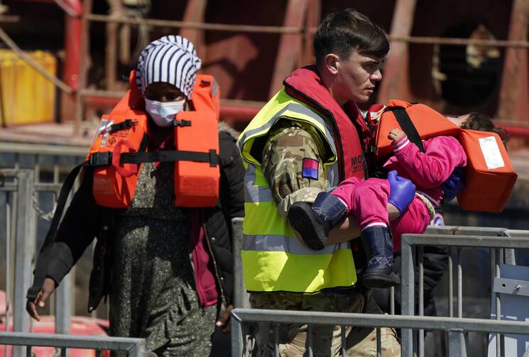 A soldier carries a child from among a group of people believed to be migrants to shore in Dover, England, after a small boat incident in the Channel, on June 14, 2022. (Andrew Matthews/PA via AP)