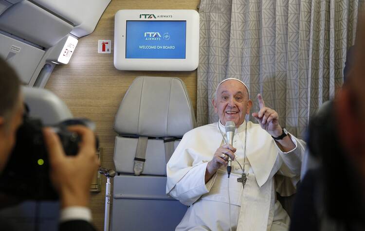 pope gestures in front of a screen on a plane that says welcome on board