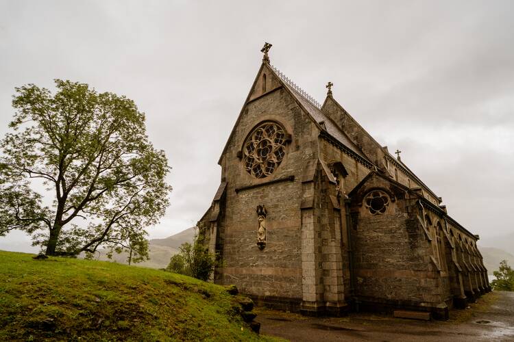 church building with a gray sky behind it and a green tree and hill to the left