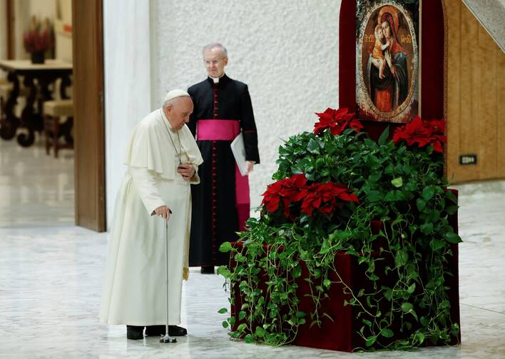 pope francis stands in front of a picture of mary, there are flowers between him and the image