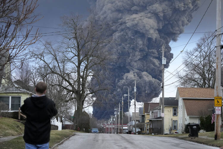 A man takes photos as a black plume rises over East Palestine, Ohio, as a result of a controlled detonation of a portion of the derailed Norfolk Southern trains.