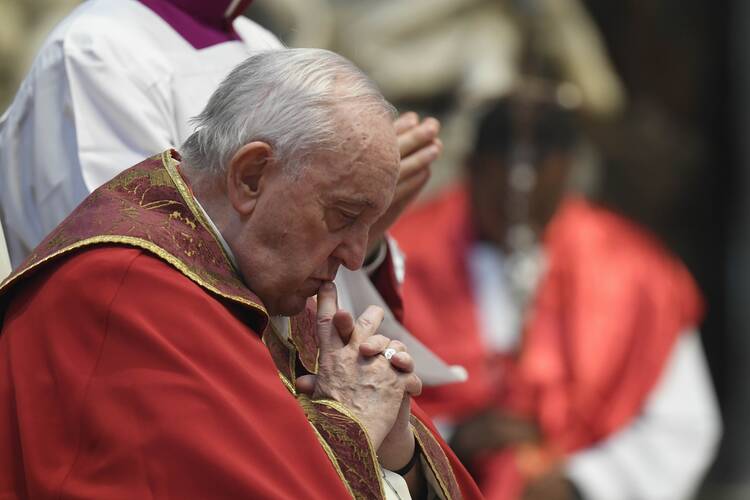 The pope, wearing red garments, bows his head in prayer