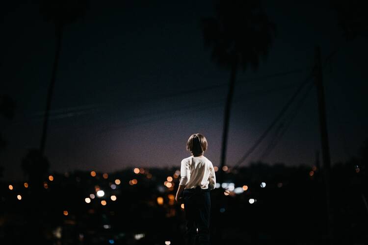 child standing in a white t-shirt looking out on a city