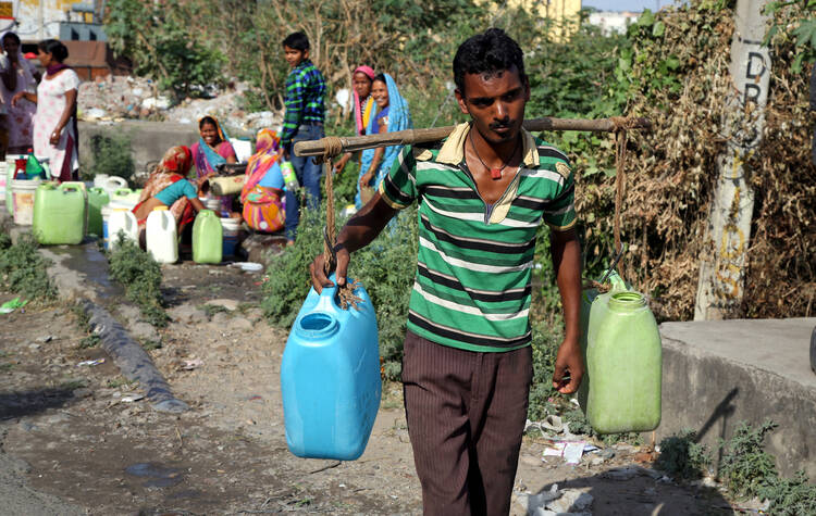 A man carries containers filled with drinking water after taking it from a public tap at a roadside in Jammu, India, May 23, 2016 (CNS photo/Jaipal Singh, EPA).