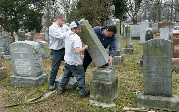 Rosenbloom Monument Co. workers from left, Nathan Fohne, Derek Doolin and Philip Weiss hoist a headstone at the Chesed Shel Emeth Cemetery in University City, Mo., where over 150 headstones were tipped over. (AP Photo/Jim Salter)