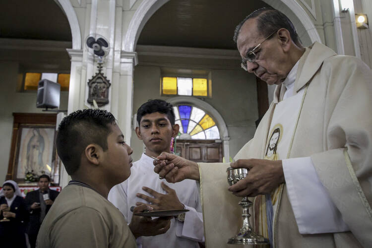 A youth takes the Eucharist from Monsignor Gregorio Rosa Chavez during a Mass giving thanks for Pope Francis' announcement that Chavez will be elevated to the rank of cardinal, at San Francisco de Asis parish church in San Salvador, El Salvador on Monday, May 22, 2017. (AP Photo/Salvador Melendez)