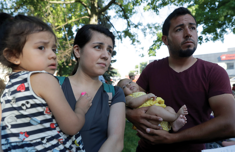 Pepe Urzua, a roofer who arrived from Mexico eight years ago, cradles his two-month-old daughter, Luna, as his wife, Betty, holds their daughter, Scarlet, during the a street festival in Goshen, Ind., on June 1, 2018. (AP Photo/Charles Rex Arbogast)