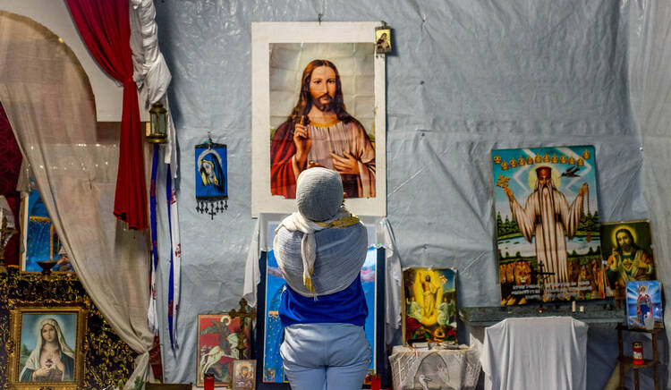 A refugee prays in front of an image of Christ in a makeshift church in a camp called "The Jungle" in 2015 in the port of Calais, France. (CNS photo/Stephanie Lecocq, EPA)