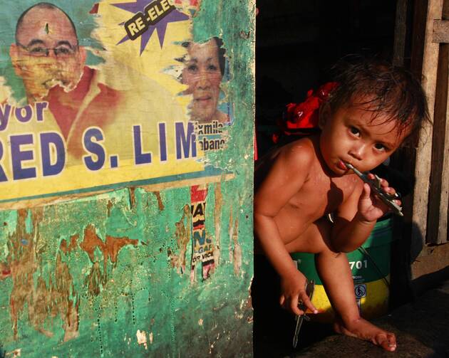A boy brushes his teeth along a road in a slum outside Manila, Philippines (CNS photo/Nicky Loh, Reuters)