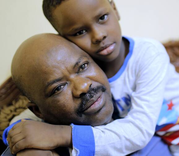 Sudanese activist Tayeb Ibrahim, who had worked to expose Sudanese abuses in the volatile South Kordofan province and hopes to see family living in the U.S. state of Iowa, is hugged by his son Mohammed during an interview with The Associated Press in Cairo, Egypt, on June 28, 2017. (AP Photo/Amr Nabil)