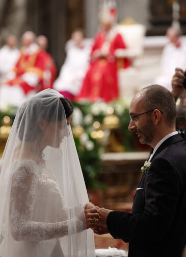 New spouses exchange rings as Pope Francis, pictured in the background, celebrates the marriage rite for 20 couples during a Mass in St. Peter's Basilica at the Vatican on Sept. 14. (CNS photo/Paul Haring)