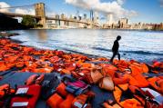 A woman in New York walks past hundreds of refugee life jackets collected from the beaches of Greece on Sept. 16, 2016. (CNS photo/Justin Lane, EPA)