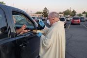 Bishop Peter Baldacchino of Las Cruces, N.M., wears a mask and gloves while giving Communion to a passenger of a vehicle during the Easter Vigil in the parking lot of the Cathedral of the Immaculate Heart of Mary in Las Cruces April 11, 2020. Bishop Baldacchino became the first-known U.S. prelate to lift a diocesan ban on public Mass April 15, 2020, and told priests they may resume sacramental ministry if they follow state health mandates. (CNS photo/courtesy David McNamara, Diocese of Las Cruces)