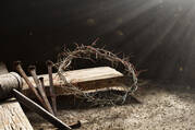 A crown of thorns and three nails rest on the edge of a wooden cross.