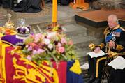 King Charles III sits in front of a coffin dressed in a military uniform