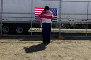 A woman prays as she faces a U.S. flag on a perimeter fence