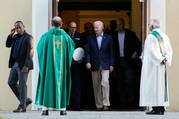 biden leaves a church and shakes the hand of a priest in green ordinary time vestments