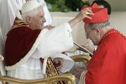 A cardinal dressed in red kneels in front of Pope Benedict XVI, seated and dressed in white