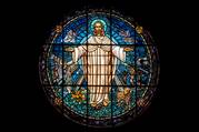 jesus stands with arms outstretched in a stained glass image