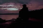 Silhouette of man sitting on rock near water during sunset