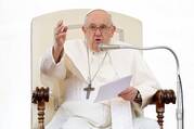 pope francis sits in his chair and gestures with his right hand while holding papers in his left