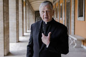 Cardinal Blase Cupich points to himself in outdoor hallway in Rome, Italy.