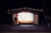 a man stands outside a backlit bus station in the dark 