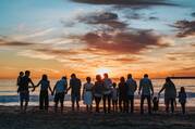 A large group of people face a sunset on the beach. 