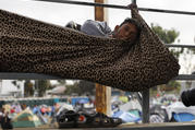 A migrant rests inside a blanket tied to keep him from rolling off the spectator stands at the Benito Juárez Sports Complex in Tijuana, Mexico. (AP Photo/Rebecca Blackwell)