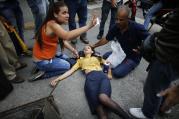 A woman is aided by fellow demonstrators after falling, overcome by tear gas, during anti-government protests in Caracas, Venezuela, Thursday, April 20, 2017. Tens of thousands of protesters asking for the resignation of President Nicolas Maduro flooded the streets again Thursday, one day after three people were killed and hundreds arrested in the biggest anti-government demonstrations in years. (AP Photo/Ariana Cubillos)