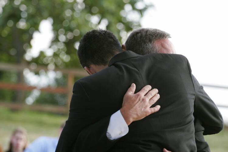 Two men in dark suits in an embrace, perhaps at a funeral