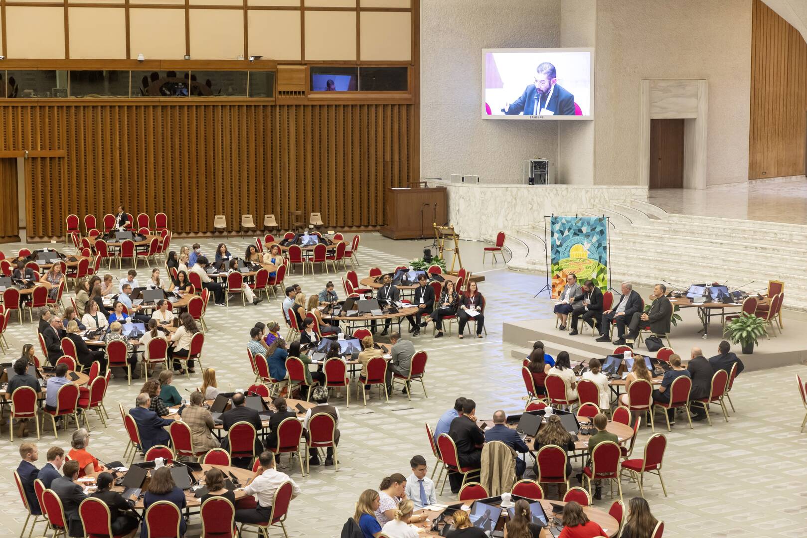 Bishop Daniel E. Flores of Brownsville, Texas, seated on stage and seen on a large screen, responds to questions from U.S. university students about the Synod of Bishops in the Paul VI Audience Hall at the Vatican Oct. 18, 2024. (CNS photo/Pablo Esparza)