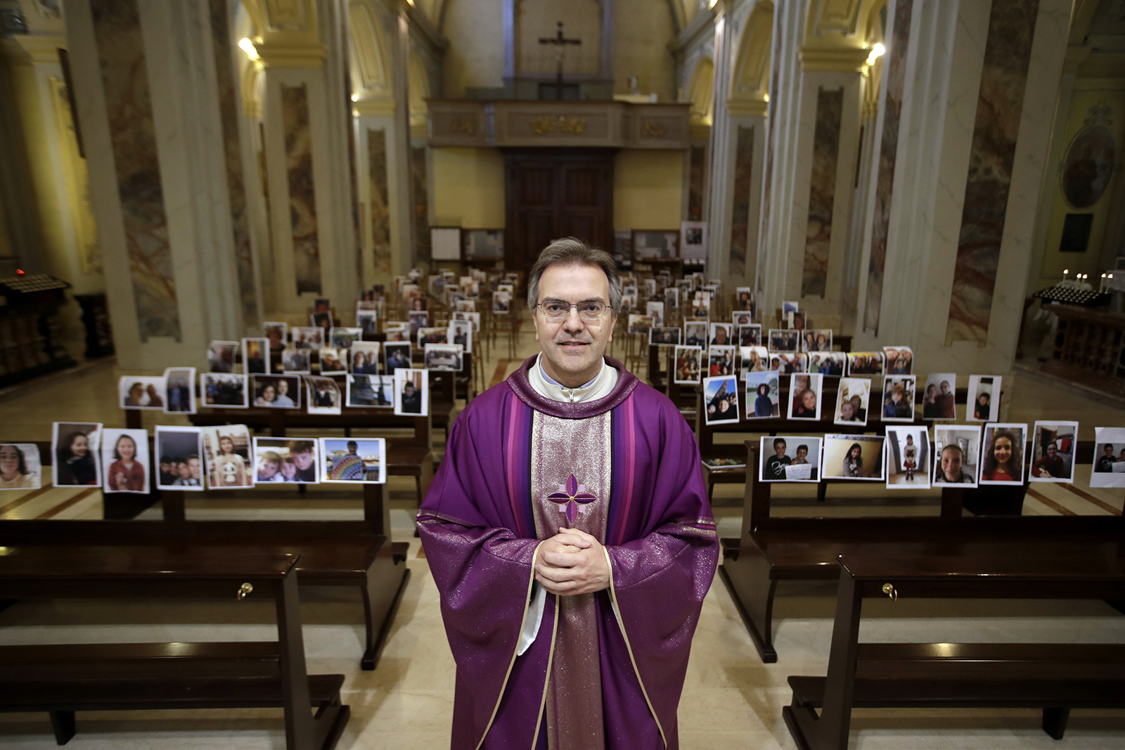 Don Giuseppe Corbari, poses in front of selfies he was sent by parishioners as Masses for the faithful have been suspended following Italy's coronavirus emergency, in Giussano, northern Italy, Sunday, March 15, 2020. (AP Photo/Luca Bruno)