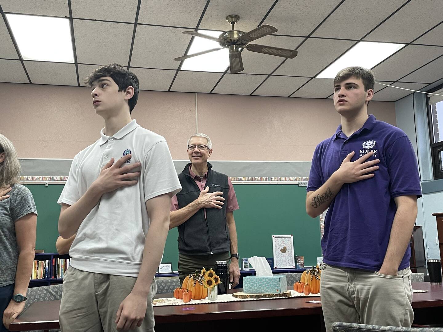 two students stand with their hands on hearts with a teacher behind them as they recite a pledge