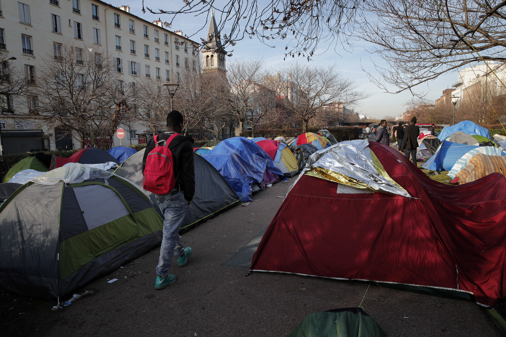 A makeshift camp in Saint Denis, outside Paris, Dec. 14, 2016. The author’s parish church is in the background (AP Photo/Christophe Ena).