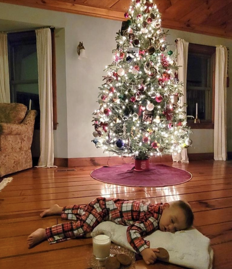 Author's god son lying on the ground in front of a Christmas tree with cookies and milk for Santa.