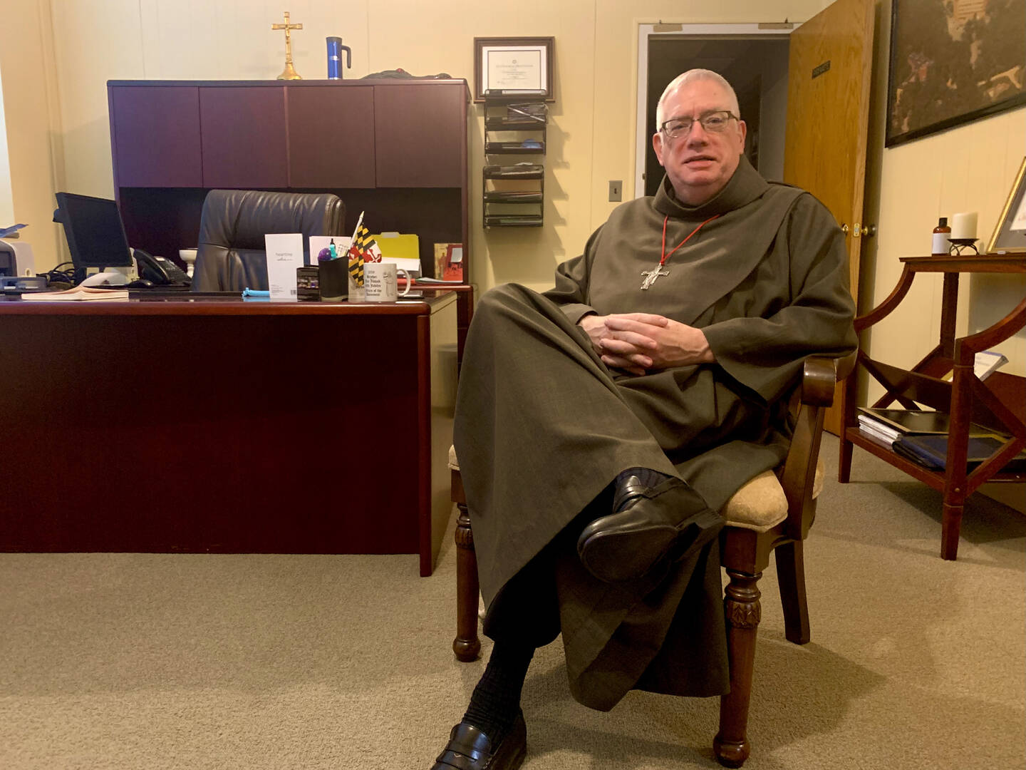 Father Loughran in his habit sitting cross-legged in a chair.
