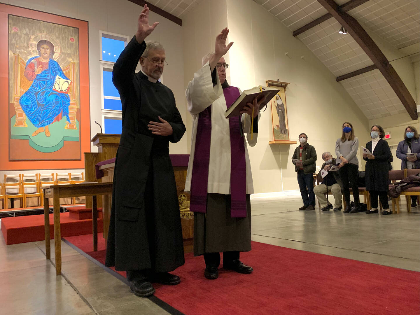 Father Steven Schunk, an Episcopalian priest, and Father Loughran raise their right hands together in blessing in front of an altar.
