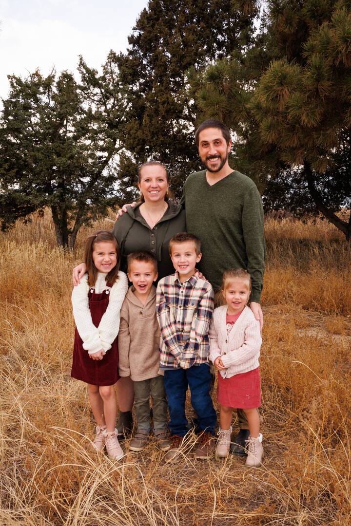 the pairitz family poses for a photo, the mother has blond hair and the father has dark hair with a beard, they have four young children