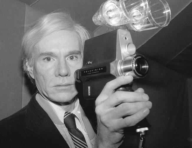 Artist and underground filmmaker Andy Warhol poses with one of Polaroid's new film cameras, the Polavision camera, which features instant replay on television screens, Feb. 1, 1978. (AP Photo/Dave Pickoff)