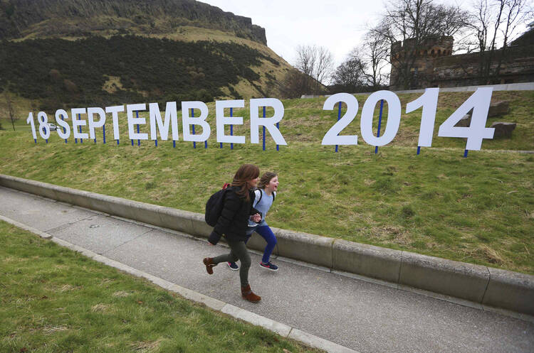 Teacher and schoolgirl run in front of sign indicating date of Scotland's independence referendum. (CNS photo/David Moir, Reuters)